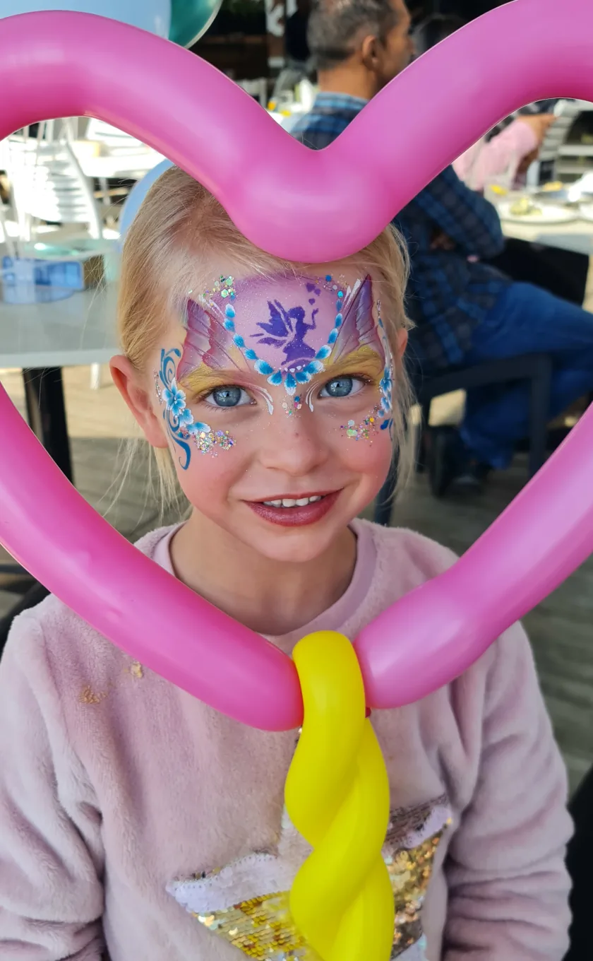 Girl with fairy face paint holding a pink heart balloon sculpture