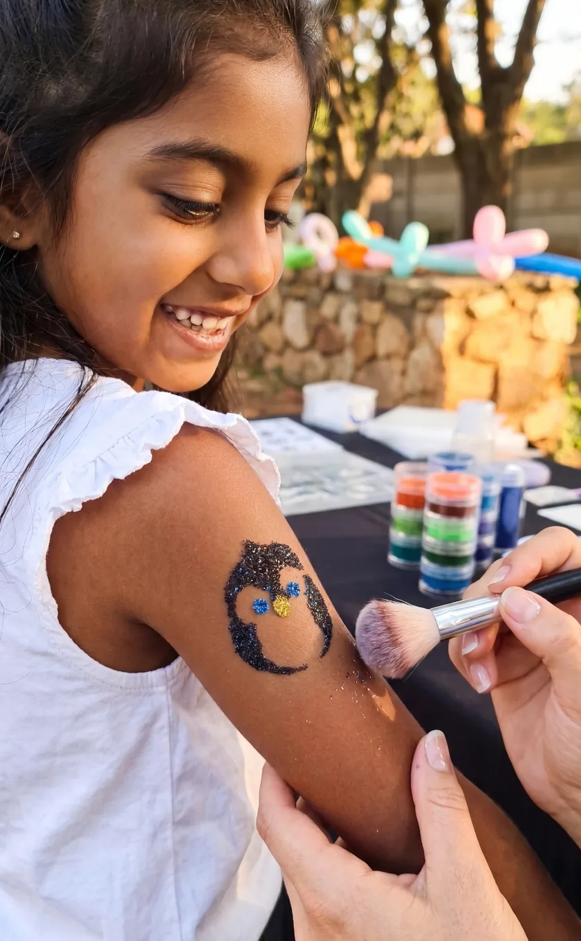 Girl getting a glitter penguin tattoo applied at a garden party