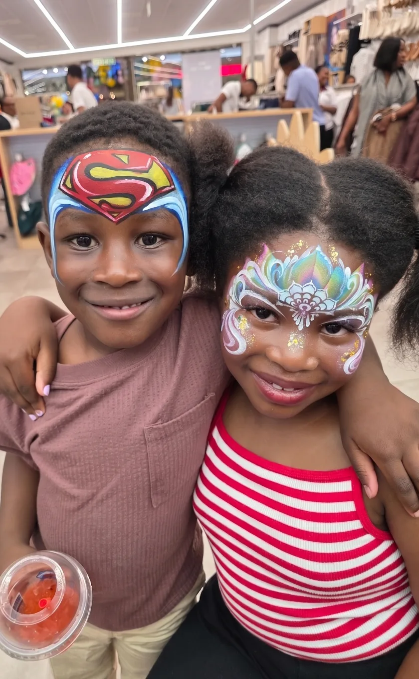 Two children with Superman and rainbow princess face paint at an event