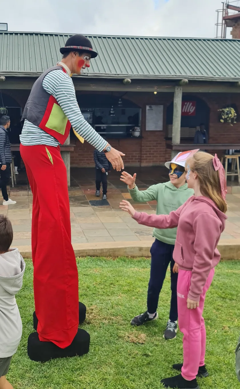 Stilt walker in clown costume greeting children at an outdoor event
